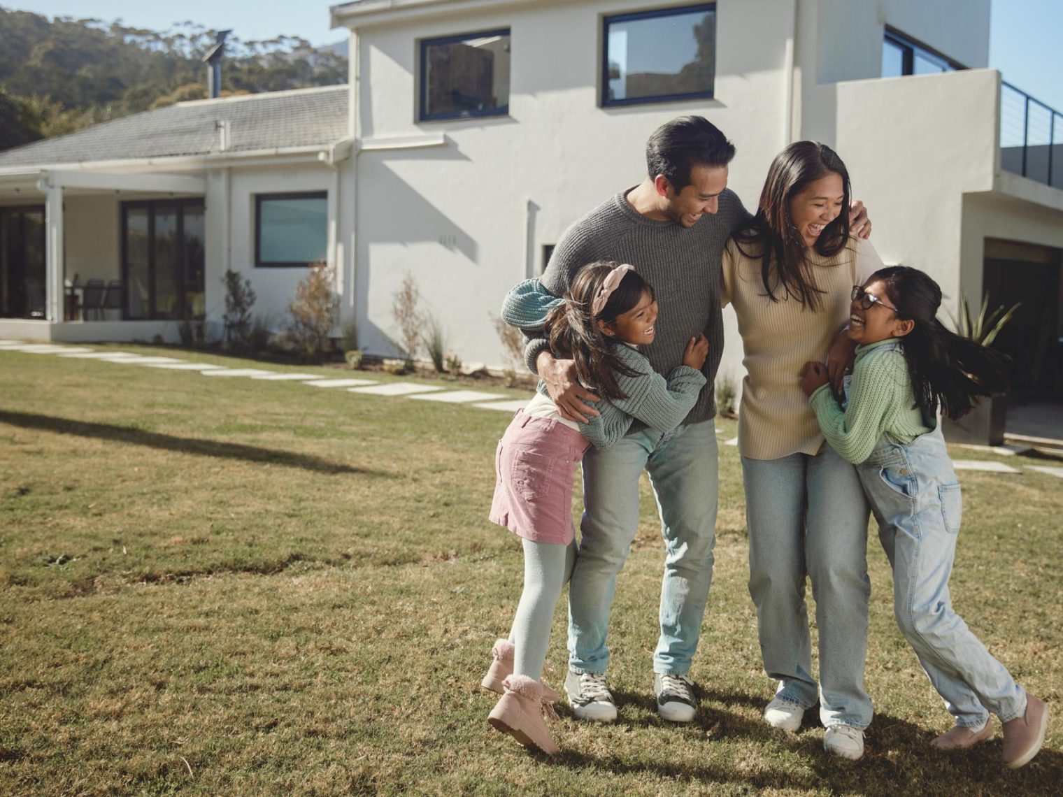 A family of four smiling and enjoying time outside their home.