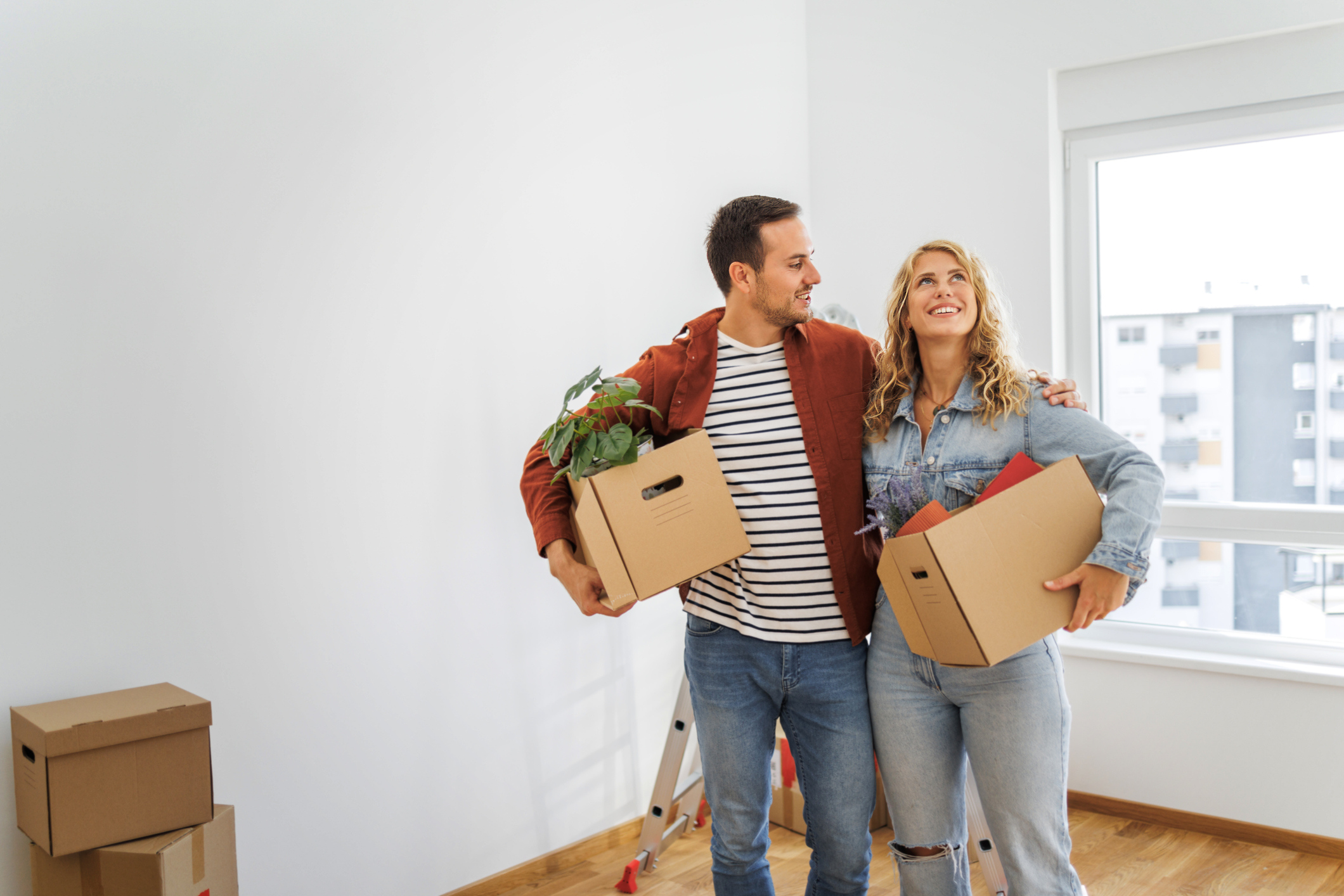 Couple holding moving boxes in the living room of a home.